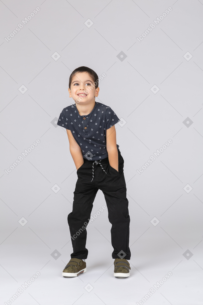 Front view of a happy boy in casual clothes posing with hands in pockets and looking at camera