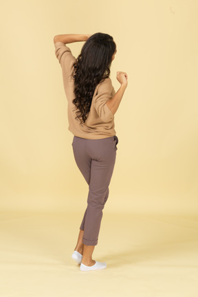 Three-quarter back view of a sleepy dark-skinned young female stretching her back