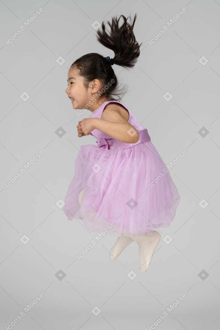 Menina de vestido rosa pulando com as pernas dobradas