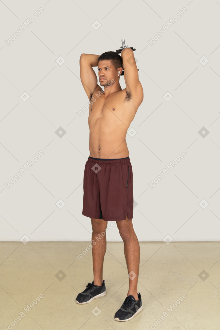 A three-quarter side view of the handsome athletic man dressed in red shorts and black sneakers doing exercises and looking to the left side