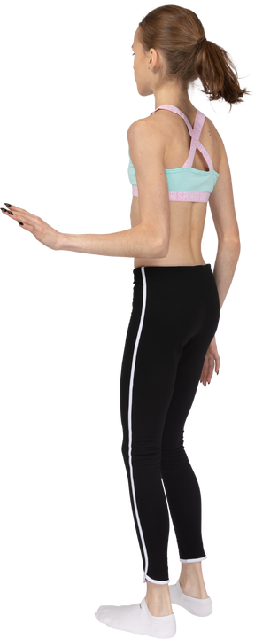Three-quarter back view of a teen girl in sportswear standing still and raising hand