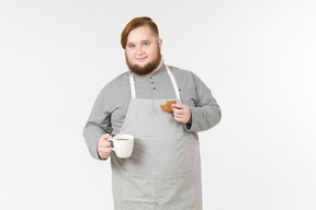 Um homem gordo segurando um cookie e uma xícara de café