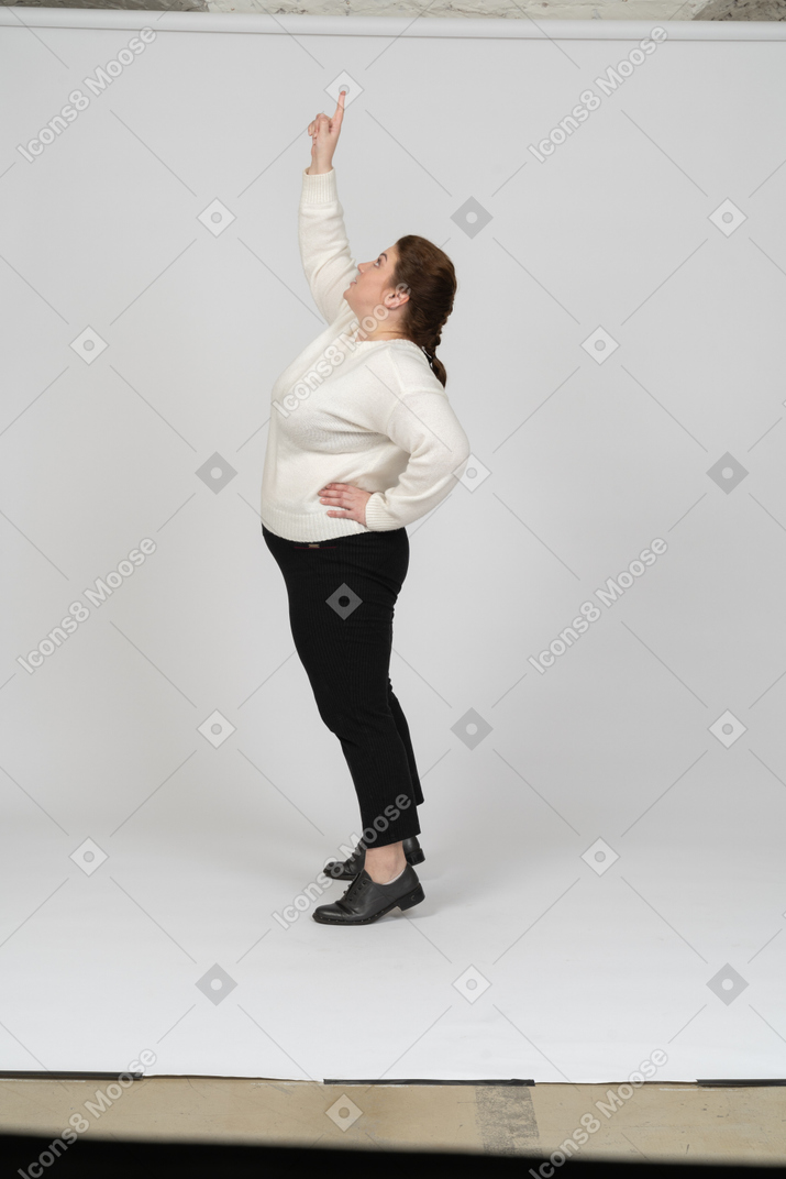 Vista lateral de una mujer regordeta en ropa casual de pie con el brazo levantado