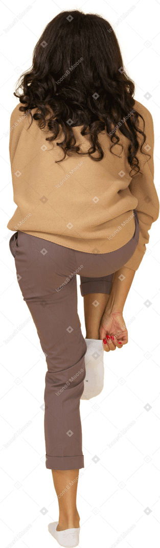 Vista posterior de una mujer joven de piel oscura cansada poniéndose un calcetín
