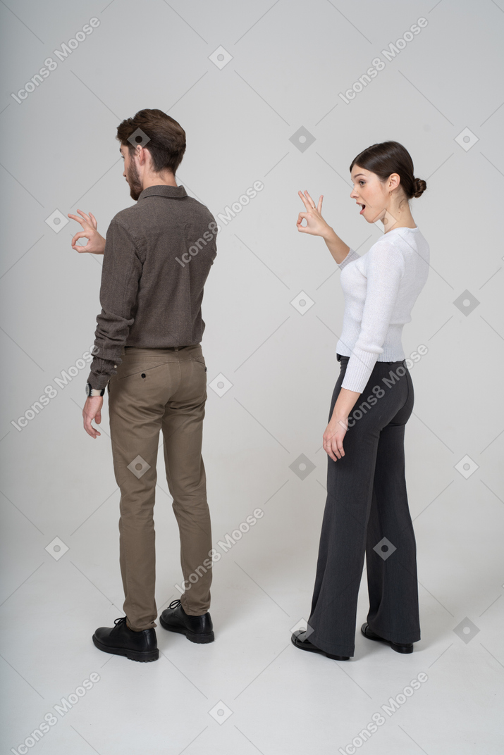 Three-quarter back view of a young couple in office clothing showing ok sign