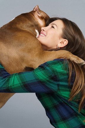 Vista lateral de una mujer sonriente en camisa de cuadros abrazando a su bulldog