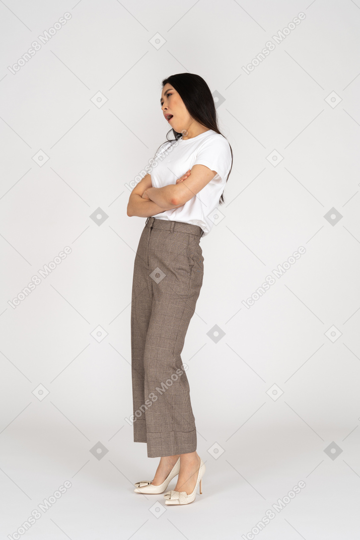 Vista di tre quarti di una giovane donna annoiata in calzoni e maglietta che incrocia le mani e inclina la testa