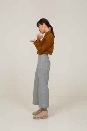 Side view of a questioning young asian female in breeches and blouse raising hands