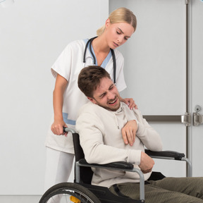A man in a wheelchair in pain being assisted by a nurse
