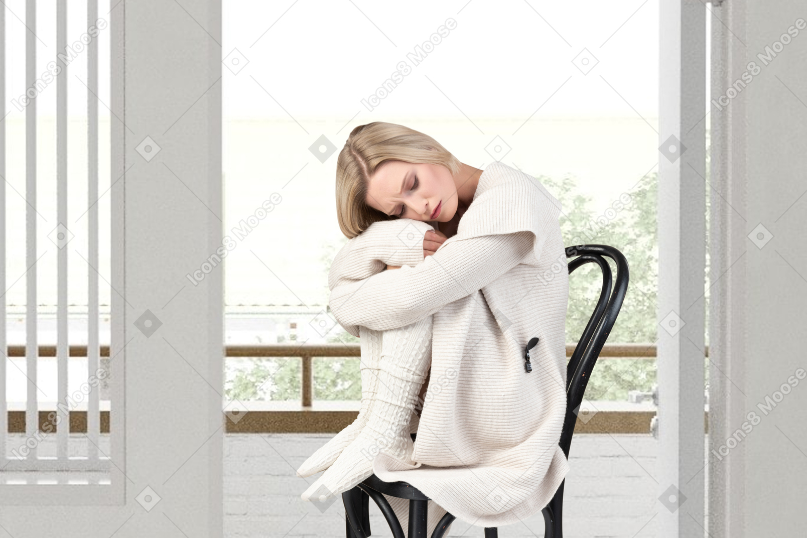 Cozy looking woman sitting on a chair next to a window and hugging her legs