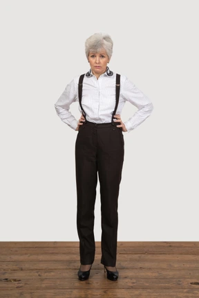 Front view of a displeased old lady in office clothing putting hands while looking at camera