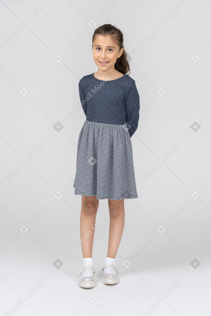 Vista frontal de uma garota sorrindo timidamente com as mãos atrás das costas