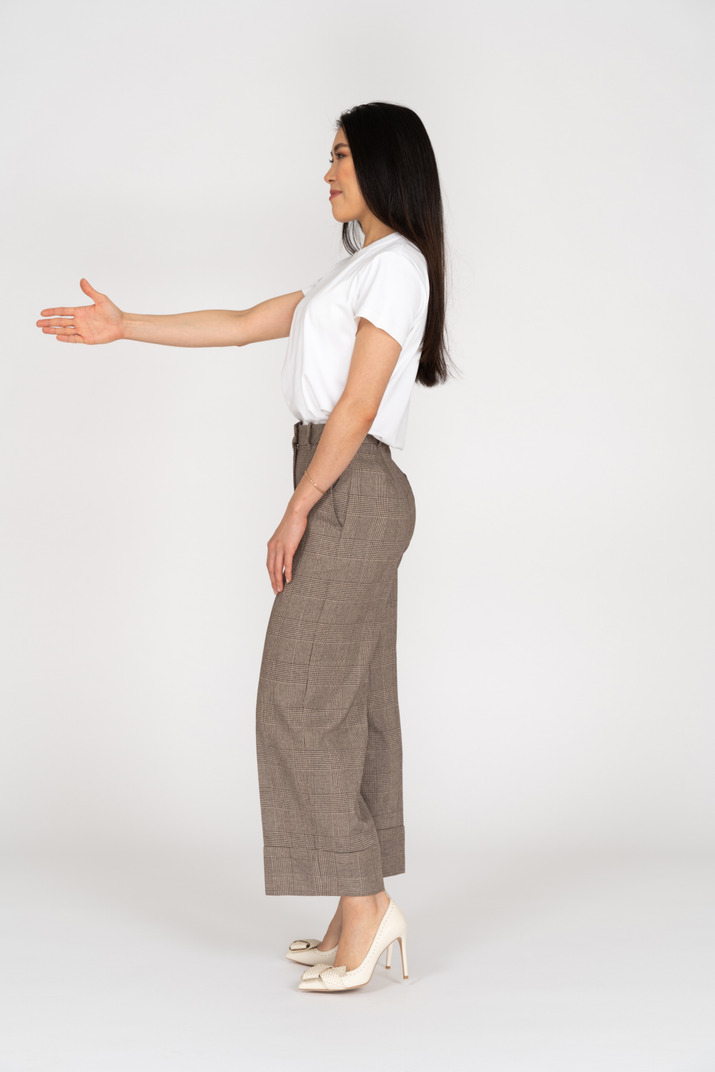 Side view of a greeting young lady in breeches and t-shirt outstretching her hand