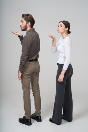 Three-quarter back view of a young couple in office clothing sending an air kiss