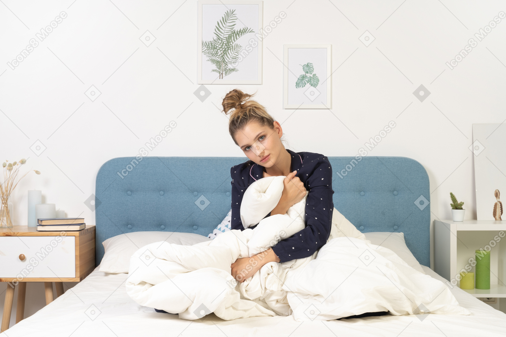 Front view of a tired young woman in pajamas with blanket staying in bed