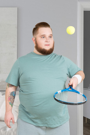A fat man holding a tennis racket and ball