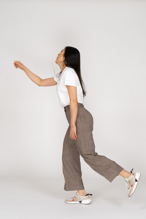 Side view of a dancing young lady in breeches and t-shirt outstretching her hand