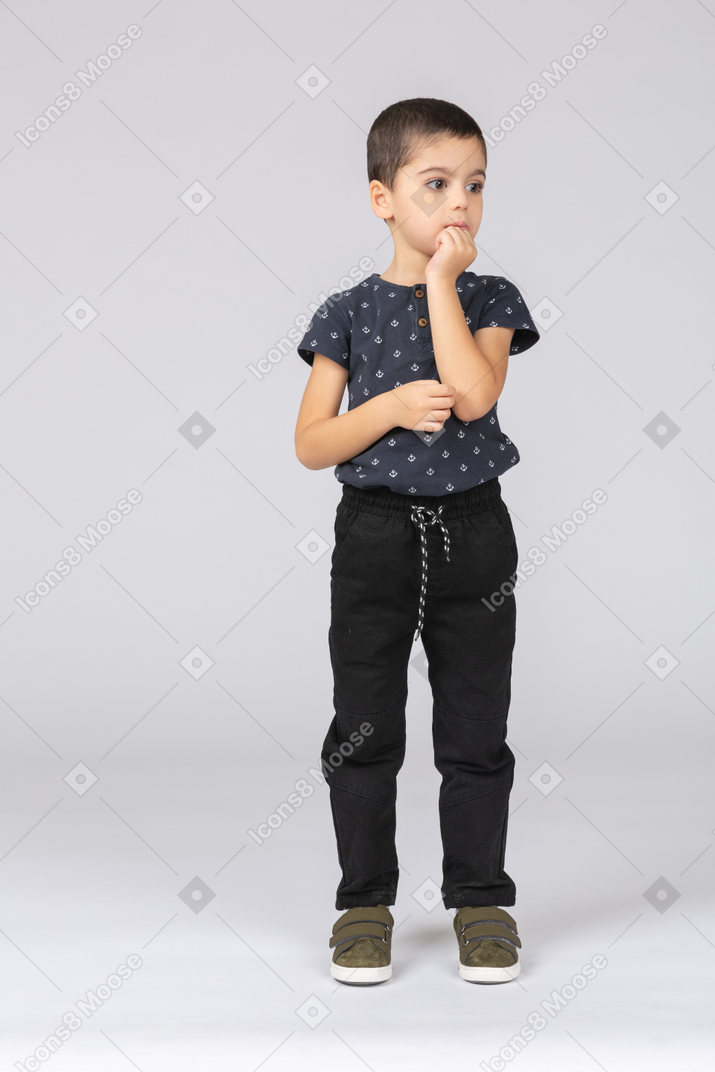 Front view of a cute boy in casual clothes posing with fist on chin