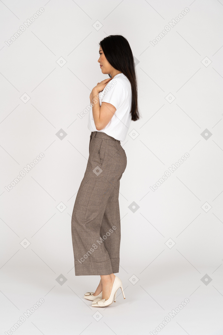 Vista laterale di una giovane donna in calzoni e t-shirt toccando il petto