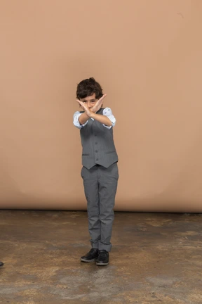 Front view of a cute boy in grey suit showing stop sign