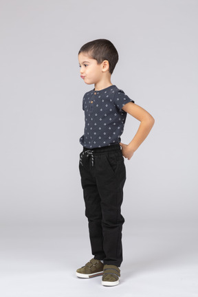 Vista lateral de un chico lindo en ropa casual posando con las manos en la espalda