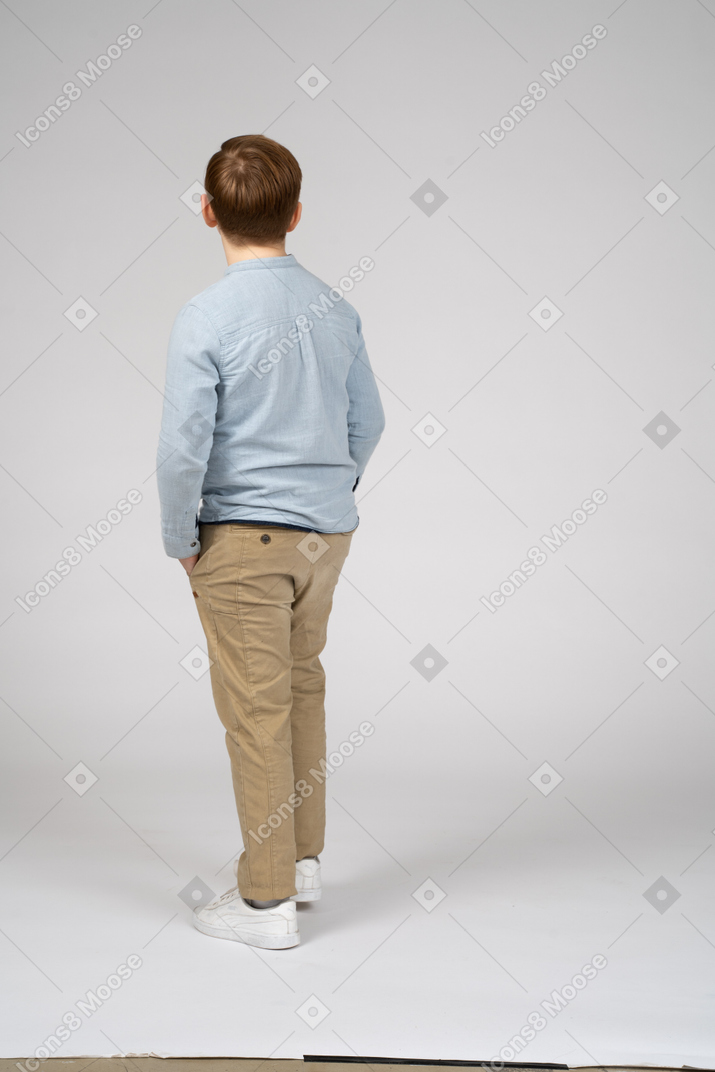Vista traseira de um menino de pé com as mãos nos bolsos