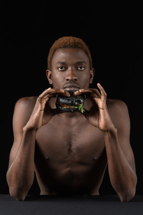 Front view of a young afro man holding a burger