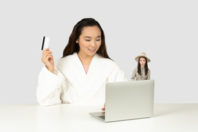 Mulher na frente do laptop segurando o cartão de crédito e sua pequena cópia