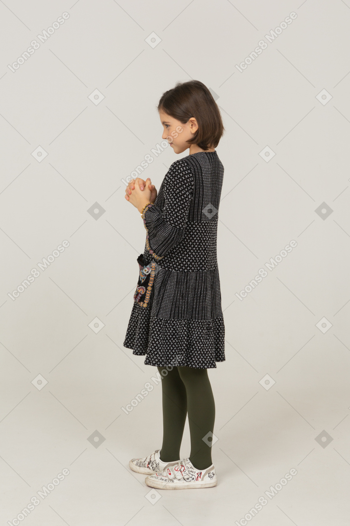 Side view of a sly little girl in dress holding hands together