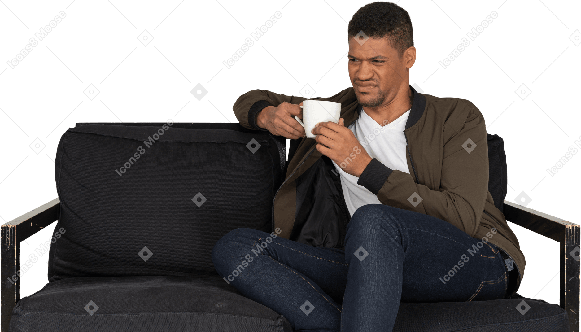 Front view of a young grimacing man sitting on a sofa with a cup of coffee