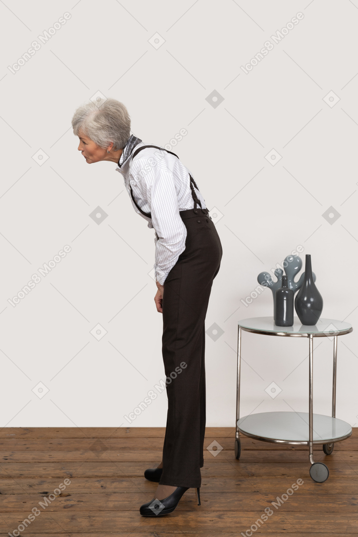 Seitenansicht einer neugierigen alten dame in bürokleidung, die sich nach vorne beugt