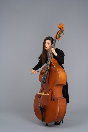 Vista de tres cuartos de una joven aburrida tocando el contrabajo