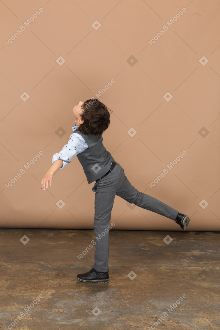 Вид сбоку на мальчика в костюме, балансирующего на одной ноге с вытянутыми руками