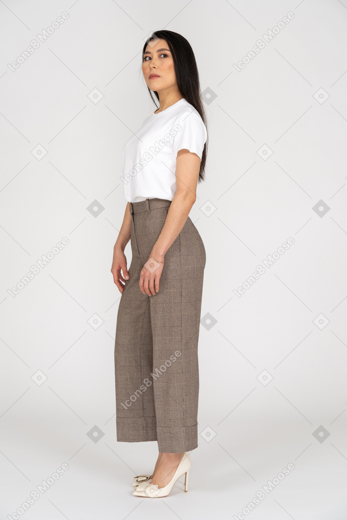 Three-quarter view of a young woman in breeches standing still while looking aside