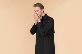 Catholic priest praying with eyes closed using prayer beads