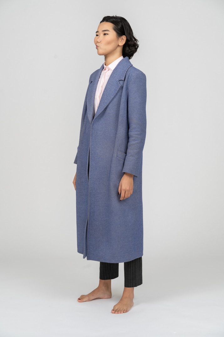 Doubting young asian woman in long blue coat standing half sideways