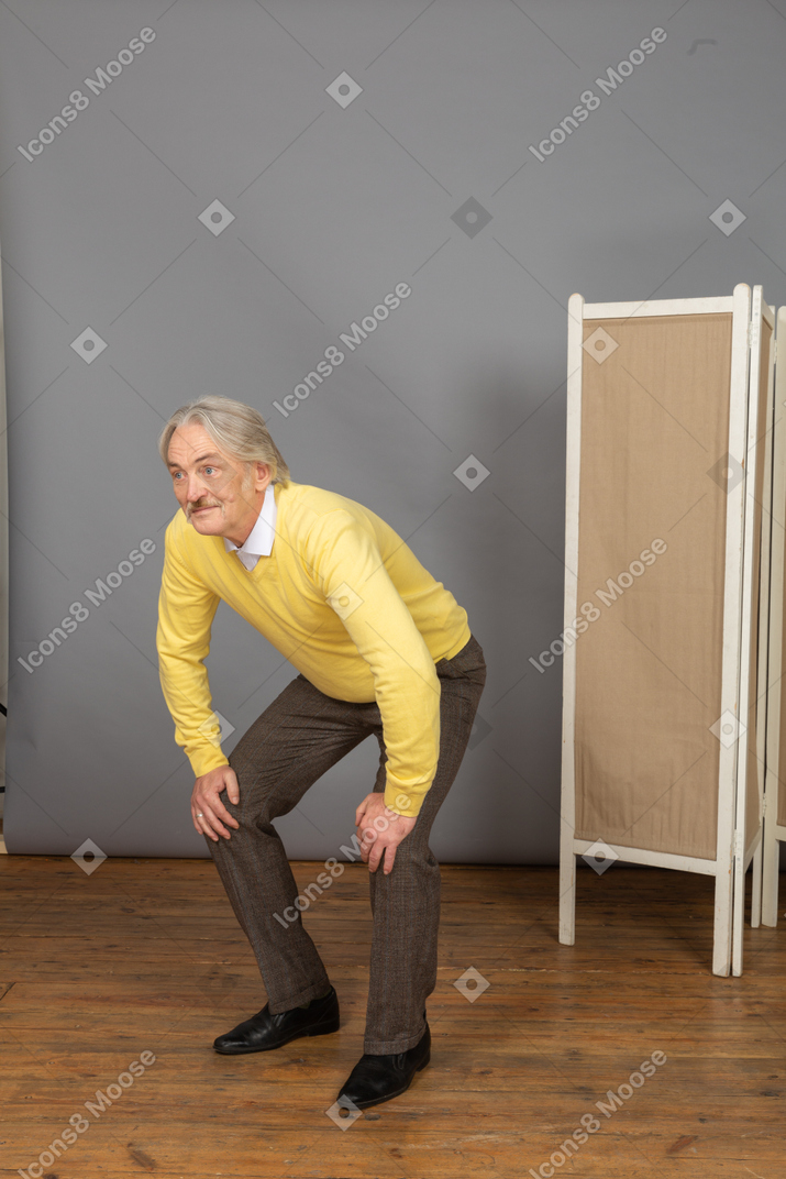 Three-quarter view of a curious old man leaning forward while putting hands on legs