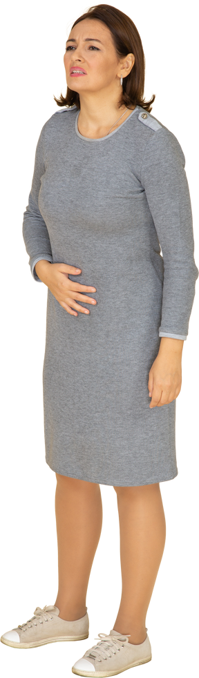 Vista frontal de uma mulher de vestido cinza sofrendo de dor de estômago