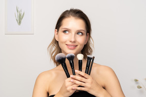 Front view of a smiling young woman holding make-up brushes and tilting head