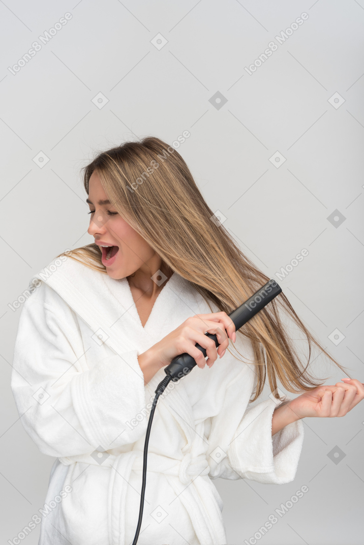 Beautiful young woman screaming while styling her hair with flat iron