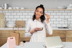 Woman holding an eyeshadow palette and applying eyeshadow 