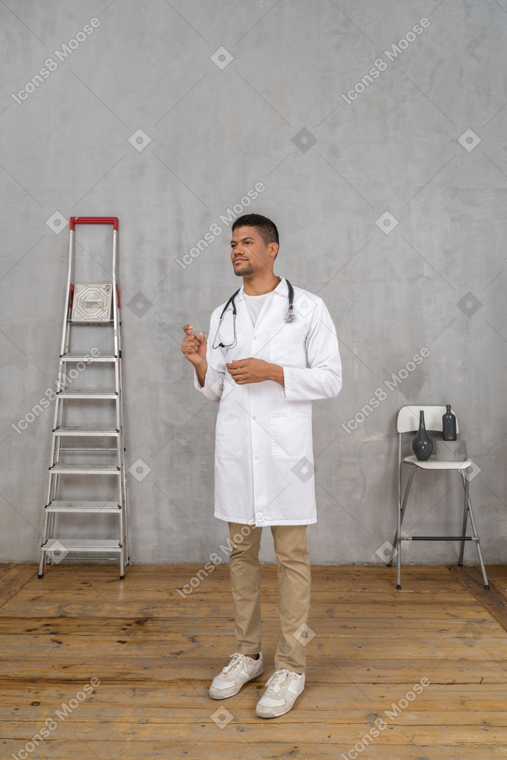뭔가의 크기를 보여주는 사다리와 의자 방에 서있는 젊은 의사의 전면보기
