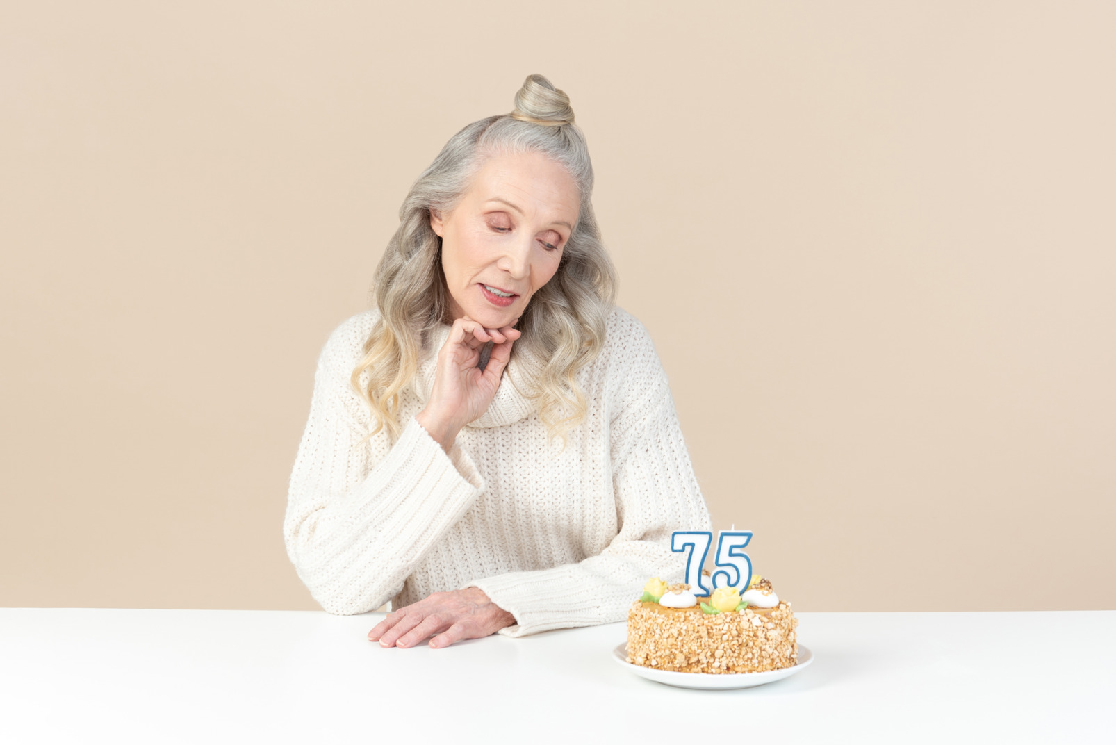 Old woman sitting at the table and looking on cake for her seventy fifth birthday