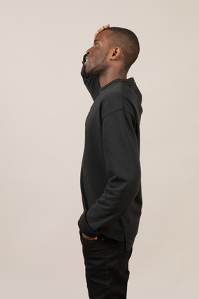 Side view of a young man looking up with hand on forehead