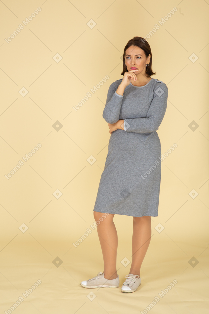 Женщина в сером платье думает, вид спереди