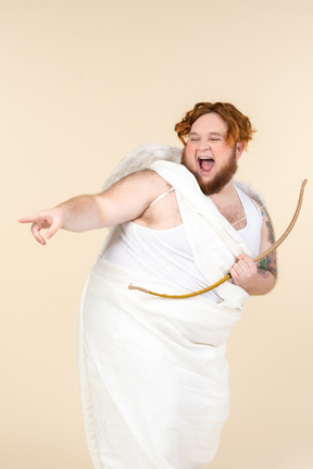 Laughing young  man dressed as a cupid holding bow and pointing