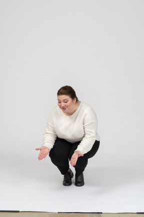 Front view of a happy plump woman in casual clothes squatting