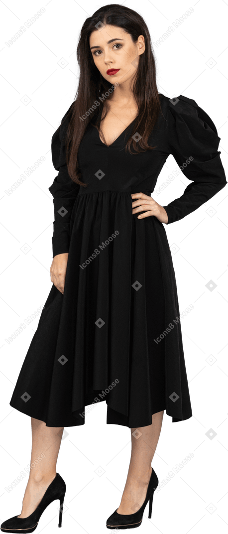 腰に手を置いている黒いドレスを着た若い女性の4分の3のビュー