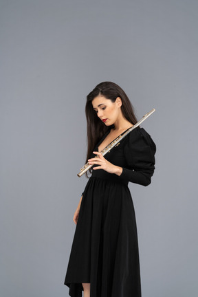 Vista de tres cuartos de una joven seria en vestido negro sosteniendo la flauta y mirando hacia abajo