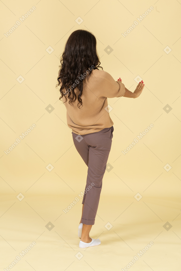 Three-quarter back view of an unwilling dark-skinned young female outstretching hands